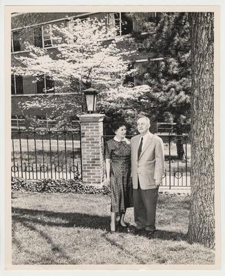 Nell Donovan (left) and President Donovan (right) are standing next to a tree at Maxwell Place.  They are near the Fine Arts Building