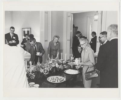 Elizabeth (Betty) Kirwan (center) is at a refreshment table, surrounded by guests, at Maxwell Place