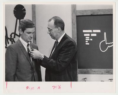 A. Rudnick (right) places a microphone on Frank Buck (left) who is teaching the distance learning class, Agriculture 106, at the UK Television Center.  University Extension was the forerunner to distance learning