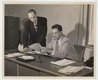 University Press Director and assistant check a proof.  Bruce Denbo (seated), director of the University of Kentucky Press, is shown here in his new campus office checking the proof for a forthcoming book.  Kenneth W. Elliott, assistant editor, is also reading the proof.  The office is in McVey Hall