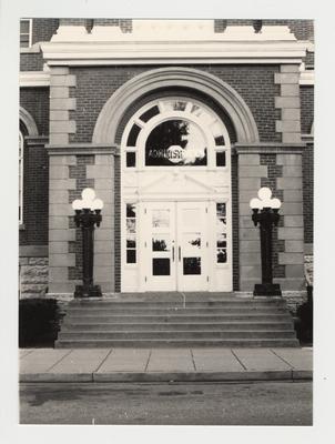 The entrance and doorway of the Administration Building from the exterior.    The glass above the door says 