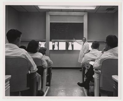 Unidentified male and female medical students are listing to an unidentified man in a classroom