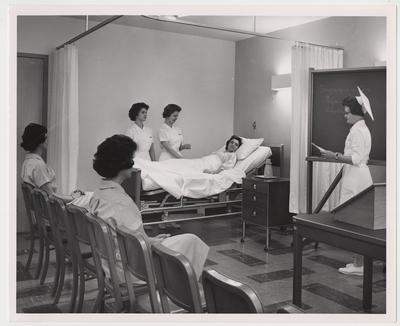 Three unidentified women are watching two unidentified women practicing hospital care with an unidentified woman