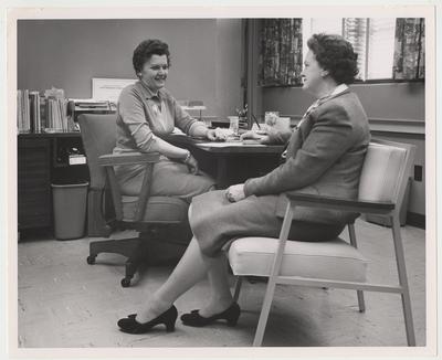 Dean Dake (left) is seated in her office talking to an unidentified woman