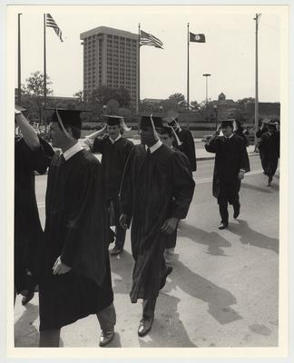 Unidentified male and female students dressed in caps and gowns are walking towards Memorial Coliseum