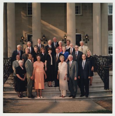 Members of the University of Kentucky administration are standing on the steps in front of Spindletop Hall.  Former Athletic Director C. M. Newton (second from left on the back row), Vice President George DeBin (next to Peggy Way), Peggy Way, secretary to President Wethington (far right, second row), Vice President Ben Carr (far right, first row), Athletic Director Larry Ivy (second from right, first row), President Charles Wethington (center, second row), Judy Wethington (center, second row, standing next to Charles Wethington), and other unidentified men and women