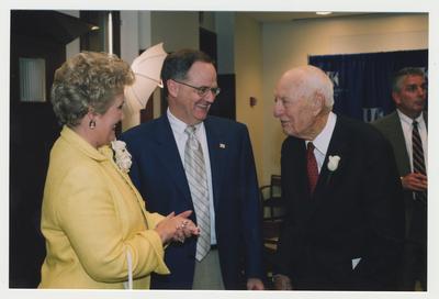 Thomas D. Clark is talking with President Lee Todd (center) and Patricia B. Todd (left) at his 100th birthday celebration at Young Library.  Carl Nathe is standing in the background to the right