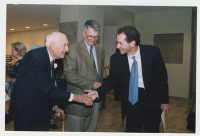 An unidentified man (right) is shaking hands with Dr. Thomas D. Clark (left) while William J. Marshall, Director of Special Collections and Archives (center) watches.  They are at Dr. Thomas D. Clark's 100th birthday celebration at Young Library