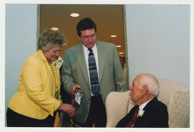 Patricia B. Todd (left) and an unidentified man (center) are giving a cane to Thomas D. Clark (right)  at Dr. Thomas D. Clark's 100th birthday celebration at Young Library