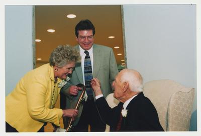 Patricia B. Todd (left) and an unidentified man (center) are giving a cane to Thomas D. Clark (right)  at Dr. Thomas D. Clark's 100th birthday celebration at Young Library
