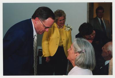 President Lee Todd (left) is talking with Loretta Brock (right)  at Dr. Thomas D. Clark's 100th birthday celebration at Young Library.  Patricia B. Todd (center, background) and an unidentified female are talking with Thomas D. Clark (right, background) in the background