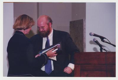Stephen Wrinn (right), Director of the University Press of Kentucky, is presenting the three millionth book to Carol Diedrichs (left), Dean of Libraries, at Dr. Thomas D. Clark's 100th birthday celebration at Young Library