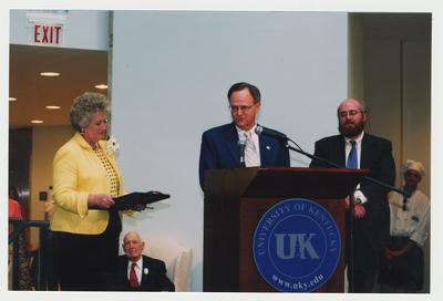 Patricia Todd (left), Thomas Clark (seated, left), Stephen Wrinn, Director of the University Press of Kentucky (right), and unidentified people are listening to President Lee Todd (center) speak at Dr. Thomas D. Clark's 100th birthday celebration at Young Library