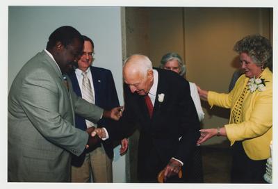 Patricia Todd (right), Loretta Brock (center, behind Clark), and President Lee Todd (second from left) are watching Thomas Clark (center) shake hands with Everett McCorvey (left), who sang Happy Birthday to Thomas Clark at Dr. Thomas D. Clark's 100th birthday celebration at Young Library