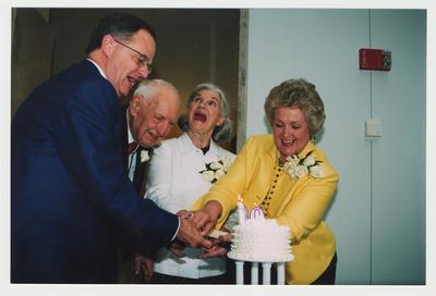Patricia Todd (right), Loretta Brock (second from right), and President Todd (left) are helping Thomas Clark (second from left) cut his birthday cake at Dr. Thomas D. Clark's 100th birthday celebration at Young Library