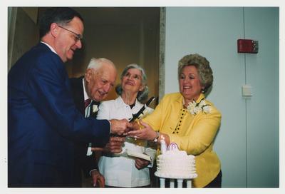 Patricia Todd (right), Loretta Brock (second from right), and President Todd (left) are helping Thomas Clark (second from left) cut his birthday cake at Dr. Thomas D. Clark's 100th birthday celebration at Young Library