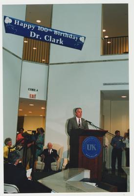 Thomas Clark (seated, center), Patricia Todd (seated, left) and unidentified people are listening to Carl Nathe, University of Kentucky Public Relations Officer, speak at Dr. Thomas D. Clark's 100th birthday celebration at Young Library