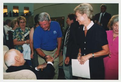 Sue Burch (right, holding paper) and Mr. Burch (left, shaking hands) are talking with Thomas Clark (seated, left) at Dr. Thomas D. Clark's 100th birthday celebration at Young Library
