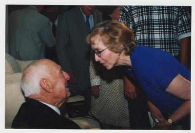 Georgeanne Strickland (right) is talking with Thomas Clark (seated, left) at Dr. Thomas D. Clark's 100th birthday celebration at Young Library