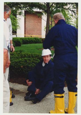 President Charles Wethington seated, putting on protective clothing as unidentified men watch. This was after the Administration Building fire