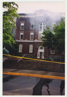 An exterior view of the Administration / Main Building during the fire.  There is an unidentified fire fighter in front of the building