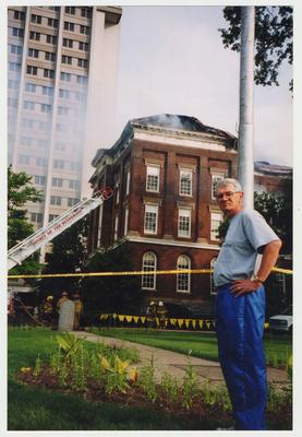 An unidentified man is standing outside of the Administration / Main Building, while unidentified fire fighters are putting out the fire