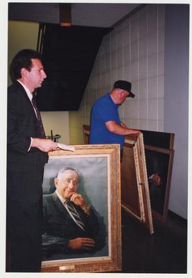 Two unidentified men are moving the painted portraits of the former presidents of the University of Kentucky