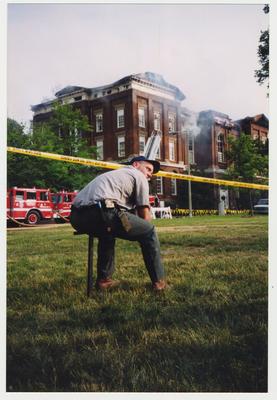 An unidentified man is seated outside of the Administration / Main Building during the fire