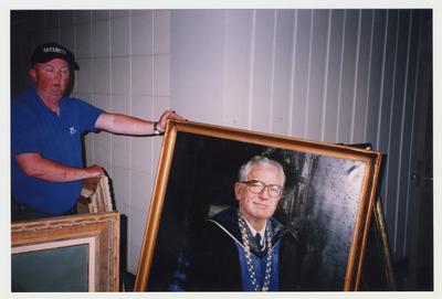 An unidentified man is holding the painted portrait of former President Otis Singletary