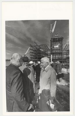 William T. Young (right, holding hat) is a donor of money to build Young Library.  He and many unidentified men are watching the construction of the William T. Young Library