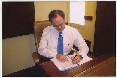President Lee Todd is seated at President Patterson's table signing some papers.  He is in a conference room located in the Main Building