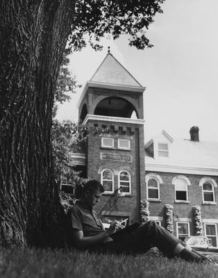 Student studying under tree in front of Mechanical Hall