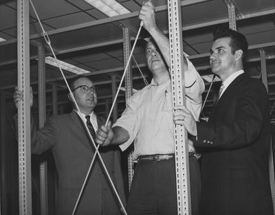 Alfred Brandon (left), Medical Librarian and Jess Martin (right), assistant Medical Librarian, watch superintendent Thomas Haskell tighten a cross brace for shelving in the UK Medical Center Science Library. Received December of 1959 from Public Relations