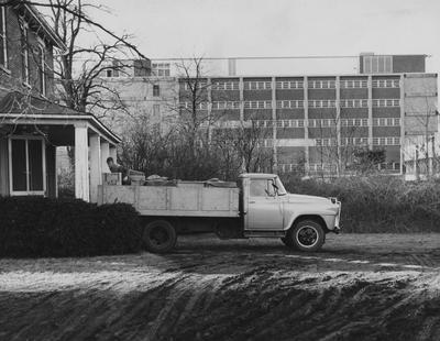 Man unloading boxes from the back of a truck onto the porch of a house, with the Medical Center in the background. Received December 16, 1959 from Public Relations