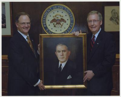 President Todd (left) and US Senator Mitch McConnell are standing with a framed portrait of United States Vice President Alben Barkley.  They are in the M. I. King Library lobby