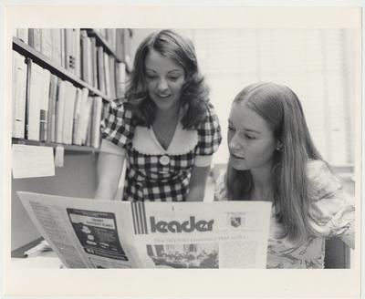 Two females, possibly students, are looking at a newspaper