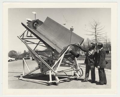 Two unidentified men are looking at a machine / equipment used for agricultural engineering