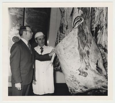 Two unidentified men are looking at meat in the animal sciences department of meat processing