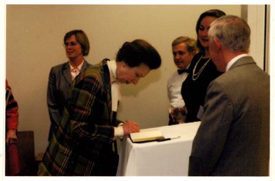 The Princess Royal Anne of Great Britain is writing something in a book as a small group of people watches