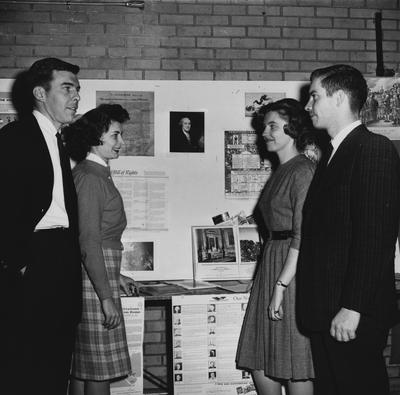 Four people standing in front of political displays. Second from left, Faye Watkins Halt. Received February 1, 1962 from Public Relations