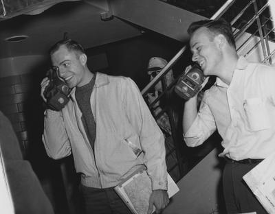 Two male students are talking on walkie talkies. The new consumer gadget is large and heavy. Unidentified man in a cap and sunglasses is watching. Received November 1, 1960 from Public Relations