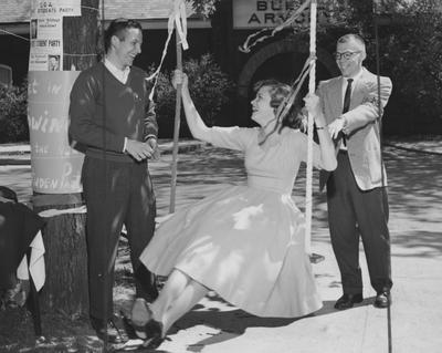 A woman swinging next to two men in front of Buell Armory. Received May 8, 1956 from Public Relations