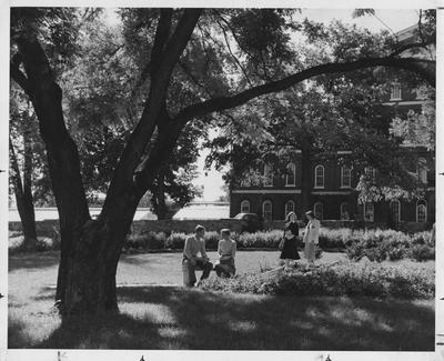 Four students socializing in the Botanical Gardens; Susan Haselden is talking to a man, and Linda Hurst (left) is talking to an unidentified woman