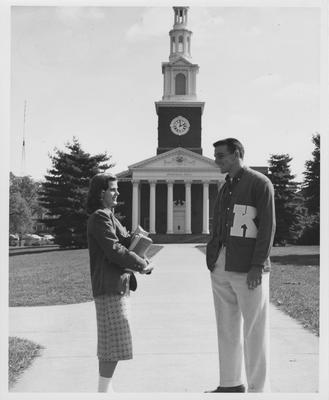Lowell Hughes is standing in front of Memorial Hall talking to an unidentified woman. Received October of 1957 from Public Relations