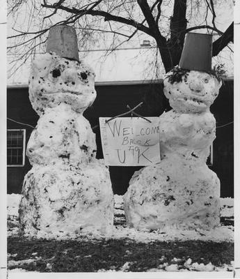 Two giant snow men with hats and a sign 