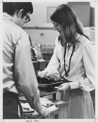 Woman handing back money to a male student in the lunch line. This image appears first on page 93 in the 1969 Kentuckian