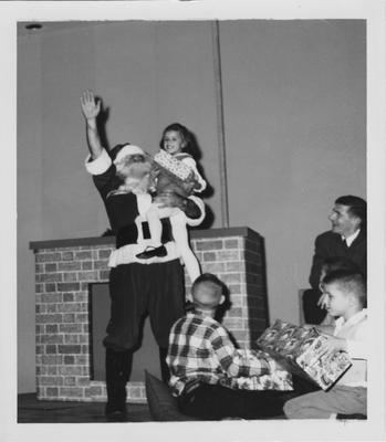 President Oswald dressed as Santa Claus handing presents to children in 1965 at Hanging of the Greens in the Student Center