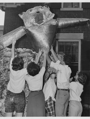 Six students and one man raise an Alumni Wildcat with papier-mâché head on either a float or house display. Lexington Herald-Leader staff photo