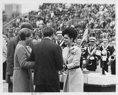 Four unidentified students and the UK band are all standing on Stoll Field at Homecoming. Appears first on page 78 in the 1969 Kentuckian