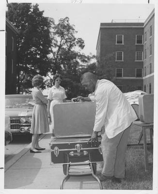 First day on campus, moving into dormitories. Two women students watch a campus employee load their luggage. This image appears third on page 27 in the 1963 Kentuckian